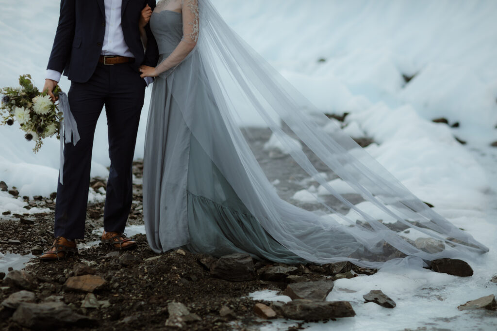 A bride in a blue wedding dress and a groom in a navy suit embrace on Matanuska Glacier in Sutton Alaska