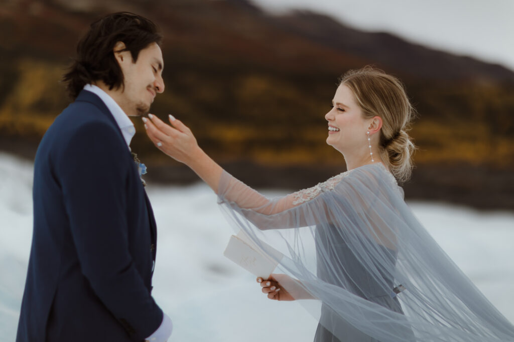 A bride in a blue wedding dress and a groom in a navy suit exchange vows on Matanuska Glacier in Sutton Alaska