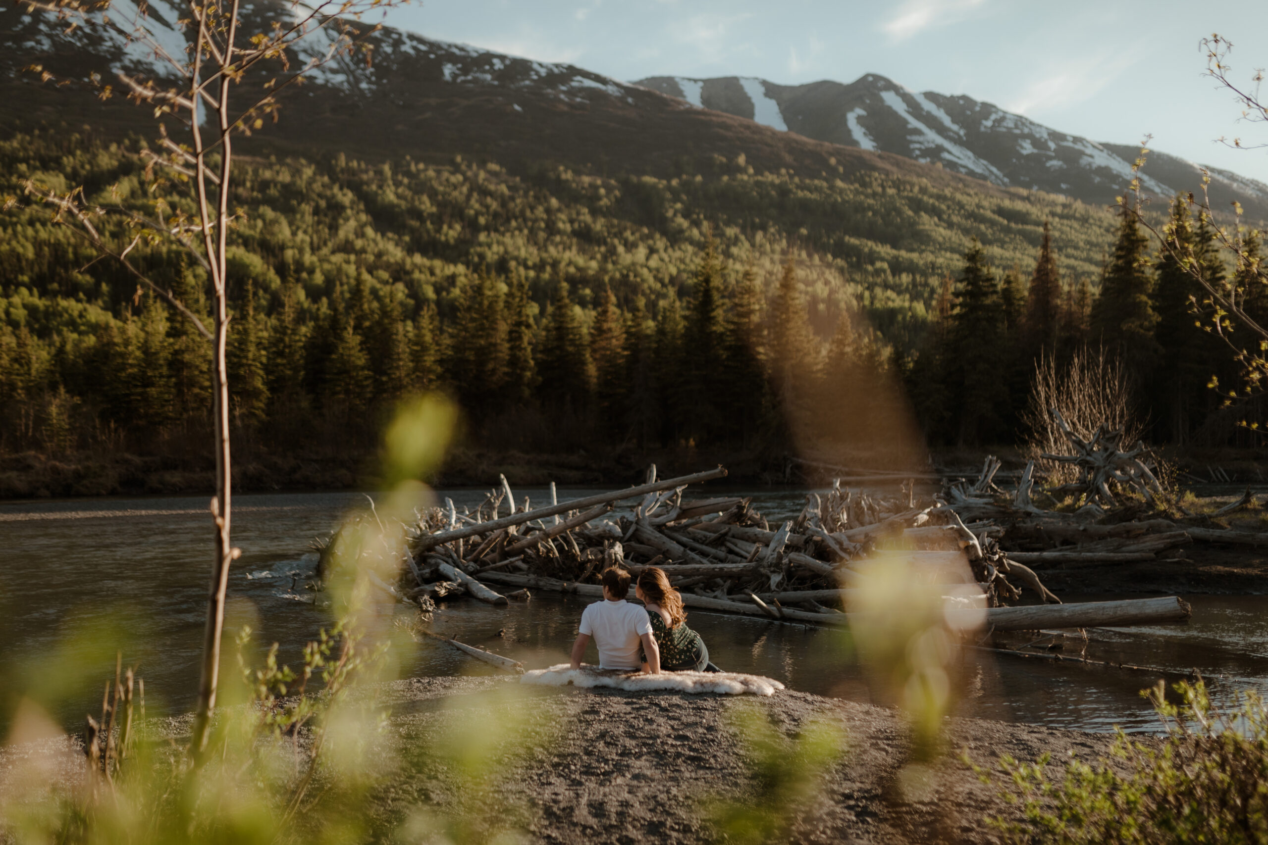 Couple with mountains behind them during golden hour sitting by river in Eagle River, Alaska