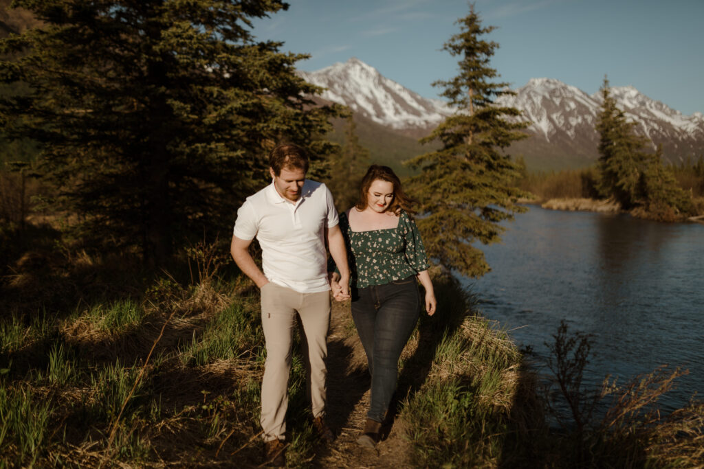 Couple with mountains behind them during golden hour walking by river in Eagle River, Alaska