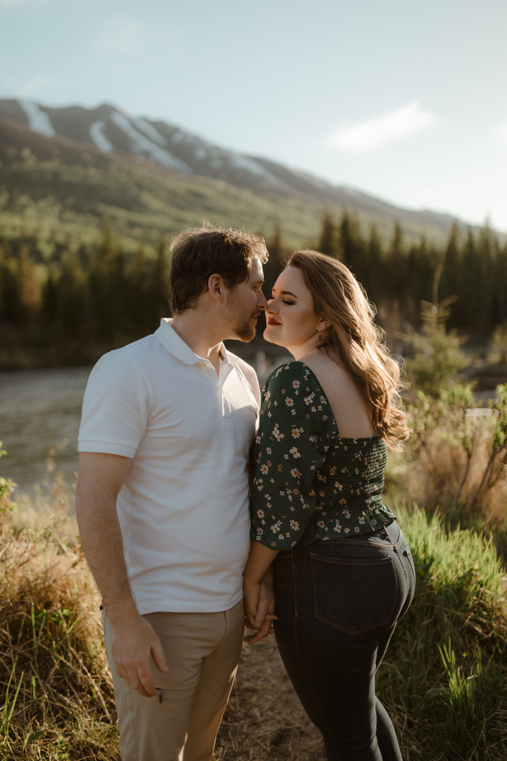 Couple with mountains behind them during golden hour embracing by river in Eagle River, Alaska