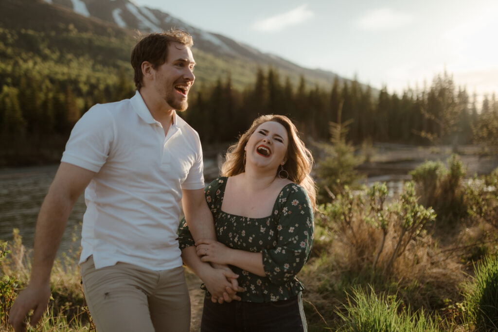 Couple with mountains behind them during golden hour laughing by river in Eagle River, Alaska