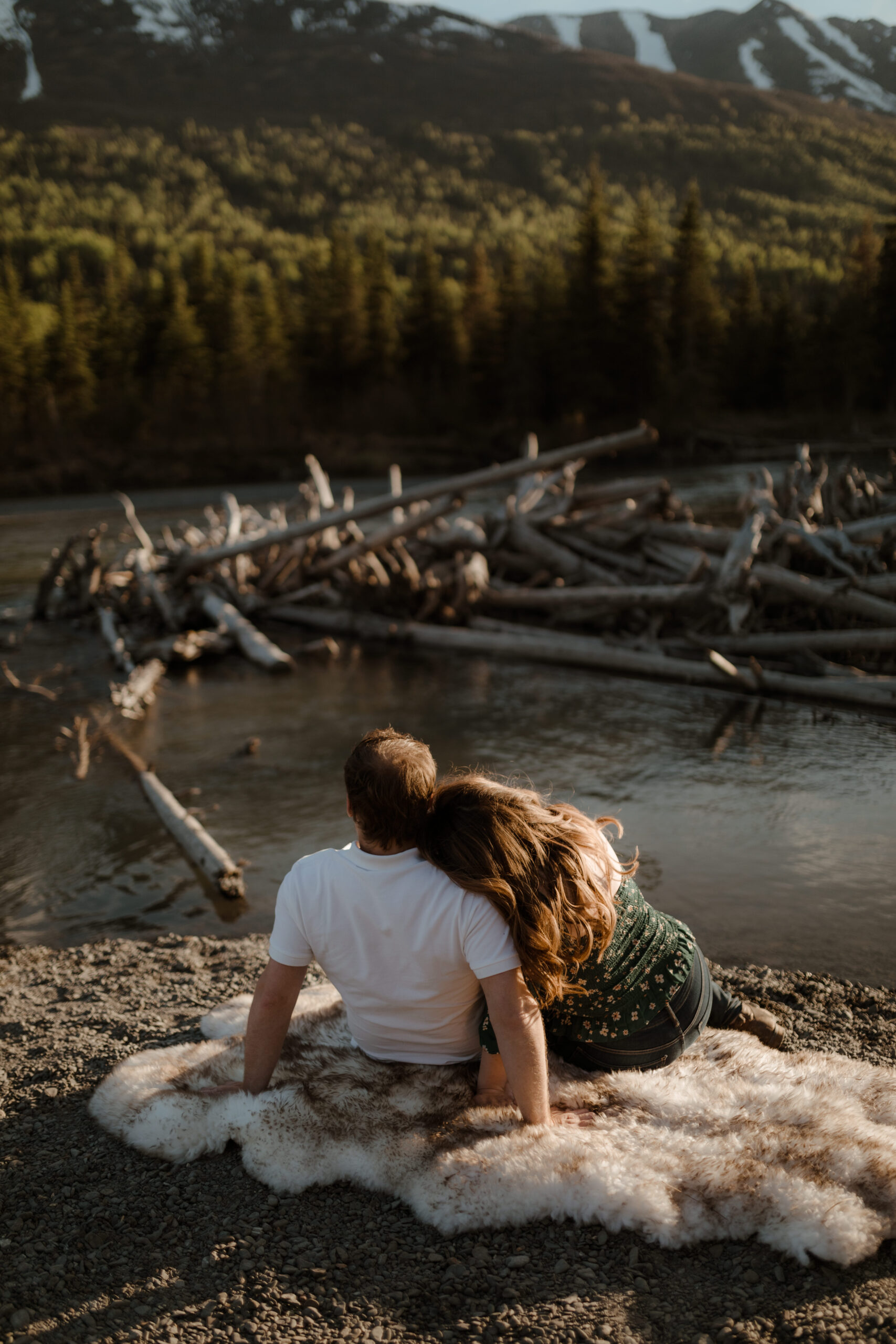 Couple with mountains behind them during golden hour sitting by river in Eagle River, Alaska