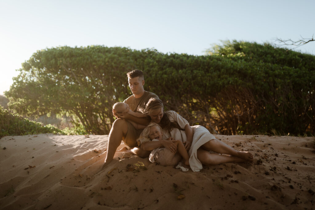 Family embracing sitting on the beach at golden hour in Maui Hawaii