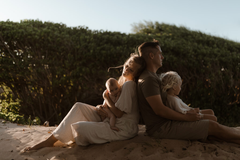 Family embracing sitting on the beach at golden hour in Maui Hawaii